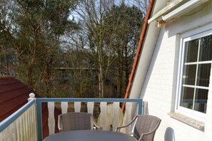 A balcony with wicker chairs, a white building, and trees in the background. - Holiday apartment with 1 bedroom (Wyk auf Föhr)
