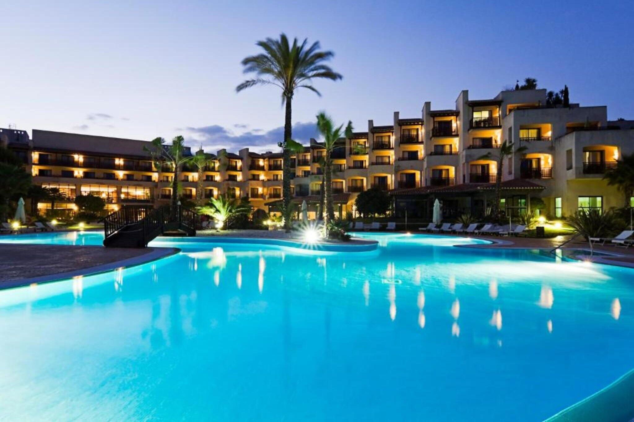 Un hotel con piscina, palmeras y varios balcones.
