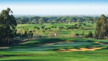 Un campo de golf con colinas ondulantes, árboles y un cielo despejado.