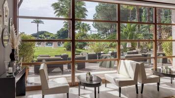 A spacious indoor area with large windows, multiple seating arrangements, and a view of a landscaped outdoor area.