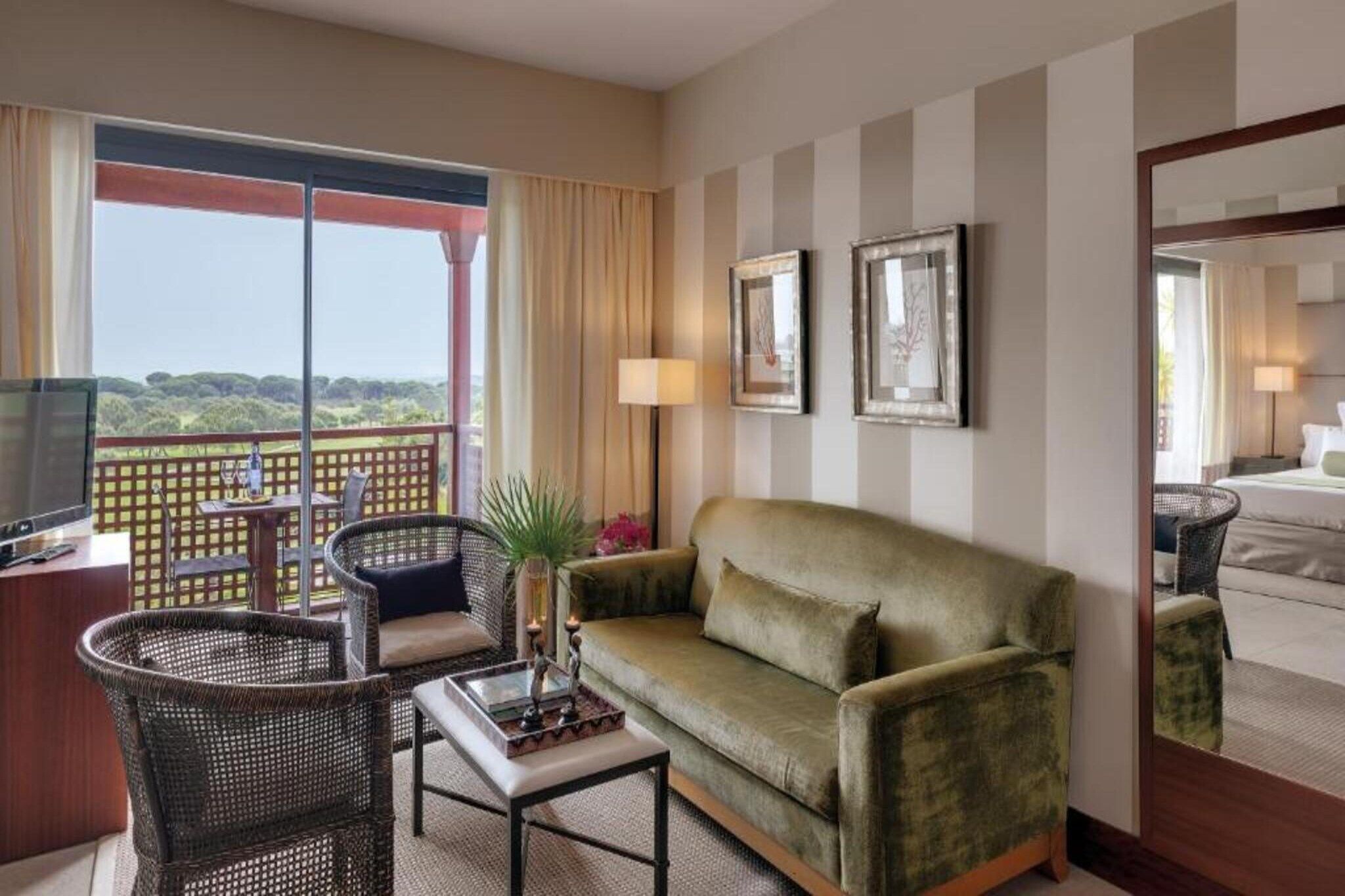 Habitación de hotel con balcón, sofá, mesa y televisión.