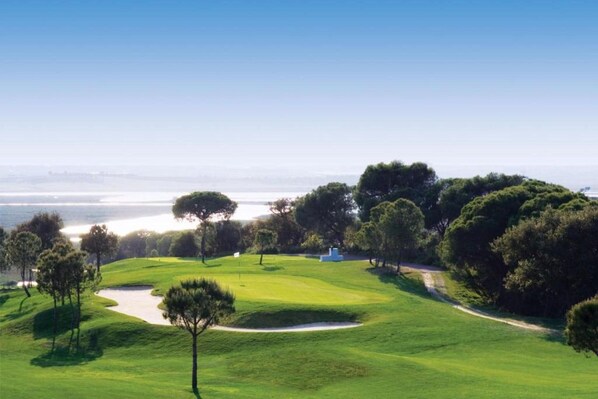 A golf course with a clear view of the ocean and a pathway leading to a building.
