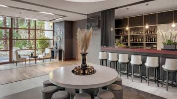 Een modern interieur met een ronde eettafel omringd door stoelen, een bar met krukken en een groot raam met uitzicht op groen.