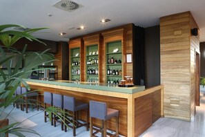 A modern bar area with a wooden counter, green shelves, and bar stools.
