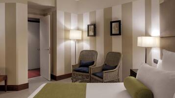 Una habitación de hotel con una cama, dos sillones de mimbre, una mesita de noche y dos lámparas de pared.