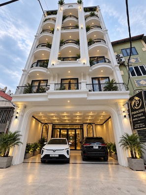A multi-story hotel with a grand entrance, two cars parked in front, and a sign indicating the name and location. - PARAGON 2 BOUTIQUE HOTEL AND POOL (Ha Noi)