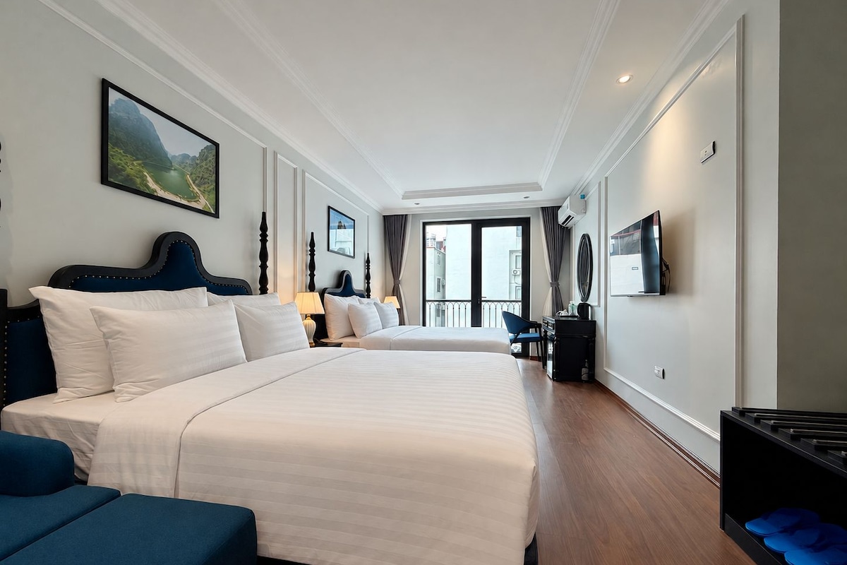 Quarto de hotel com duas camas, uma escrivaninha, uma cadeira e uma televisão.