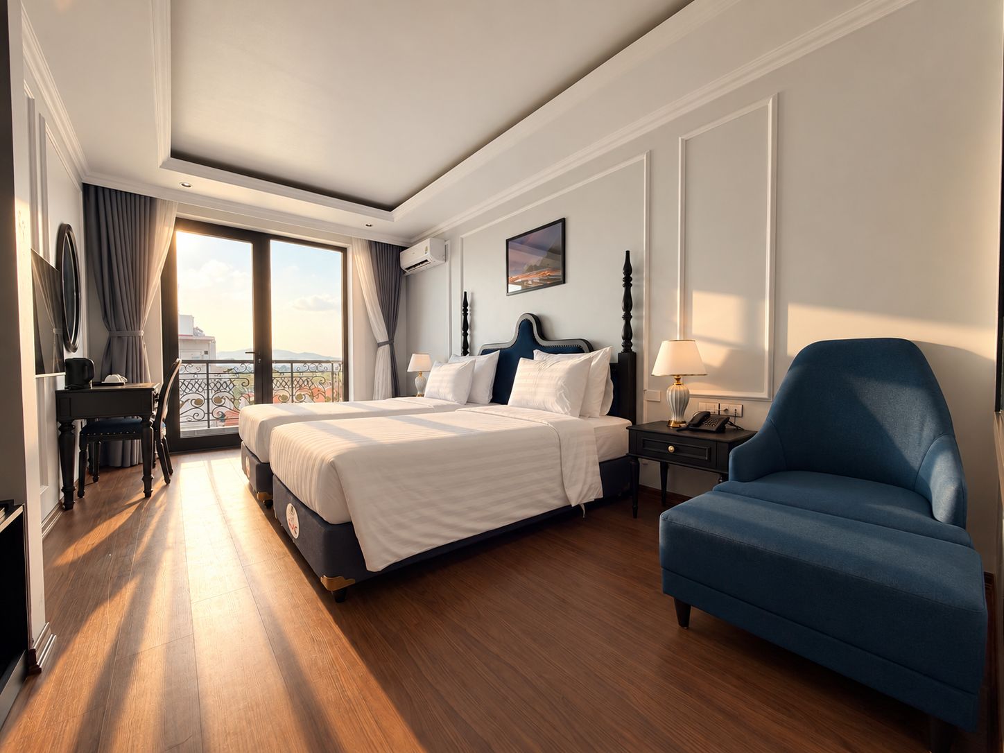 A hotel room with a large bed, a desk with a chair, a blue armchair, and a balcony with a view.