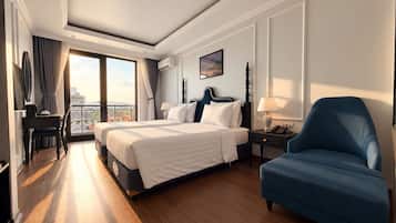 A hotel room with a large bed, a desk with a chair, a blue armchair, and a balcony with a view.