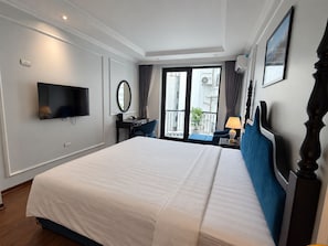 Habitación de hotel con una cama grande, un escritorio con silla, televisor, espejo y balcón con vista a la ciudad.