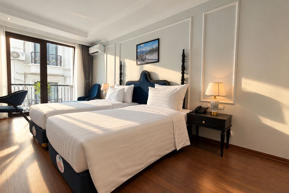Quarto de hotel com uma cama grande, uma escrivaninha, uma cadeira, um abajur e vista para o exterior.