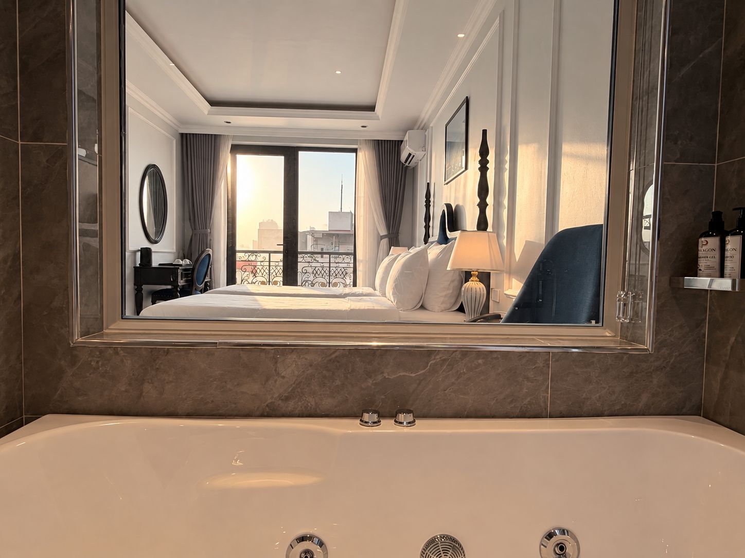Une chambre d’hôtel avec un grand lit, un coin salon, une salle de bain avec baignoire et une vue sur la ville par la fenêtre.