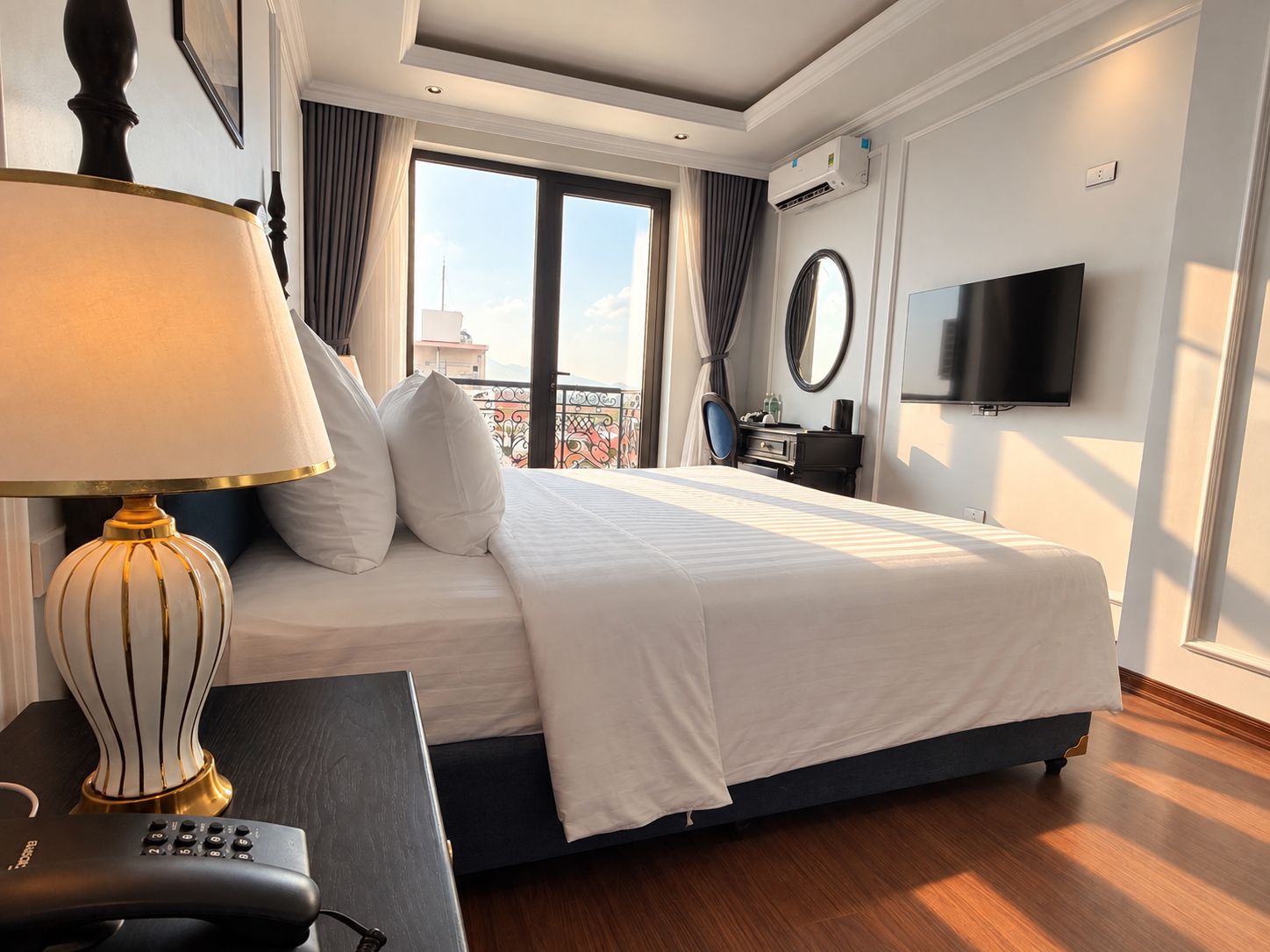 Ein Hotelzimmer mit einem Bett, einem Schreibtisch mit Lampe, einem Fernseher und Blick auf die Stadt.