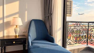 A room with a blue armchair, a lamp, and a view of a balcony with a railing.