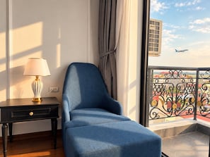 A room with a blue armchair, a lamp, and a view of a balcony with a railing. - PARAGON 2 BOUTIQUE HOTEL AND POOL (Ha Noi)