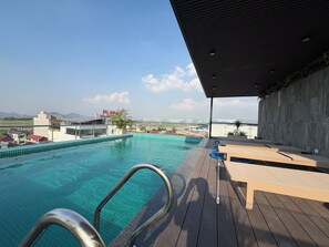 Piscina no terraço com águas azuis cristalinas, deck de madeira e vista para edifícios distantes e paisagem.