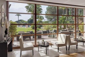 A spacious indoor area with large windows, multiple seating arrangements, and a view of a landscaped outdoor area.