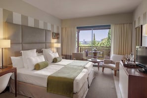 A hotel room with a large bed, a desk with a TV, a chair, and a balcony with a view.