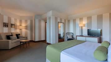 Una habitación de hotel con cama, sofá, sillón, escritorio con televisor y espejo.