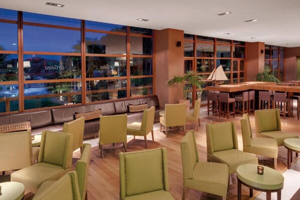 A modern lounge area with leather seating, a bar, and large windows offering a view of the cityscape.
