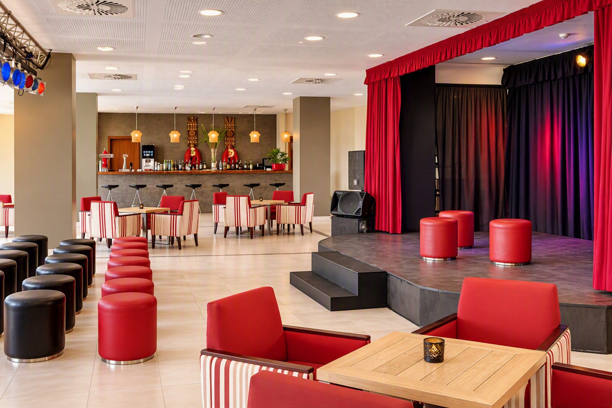 A theater with red curtains, a stage, and a bar area with stools and bottles.