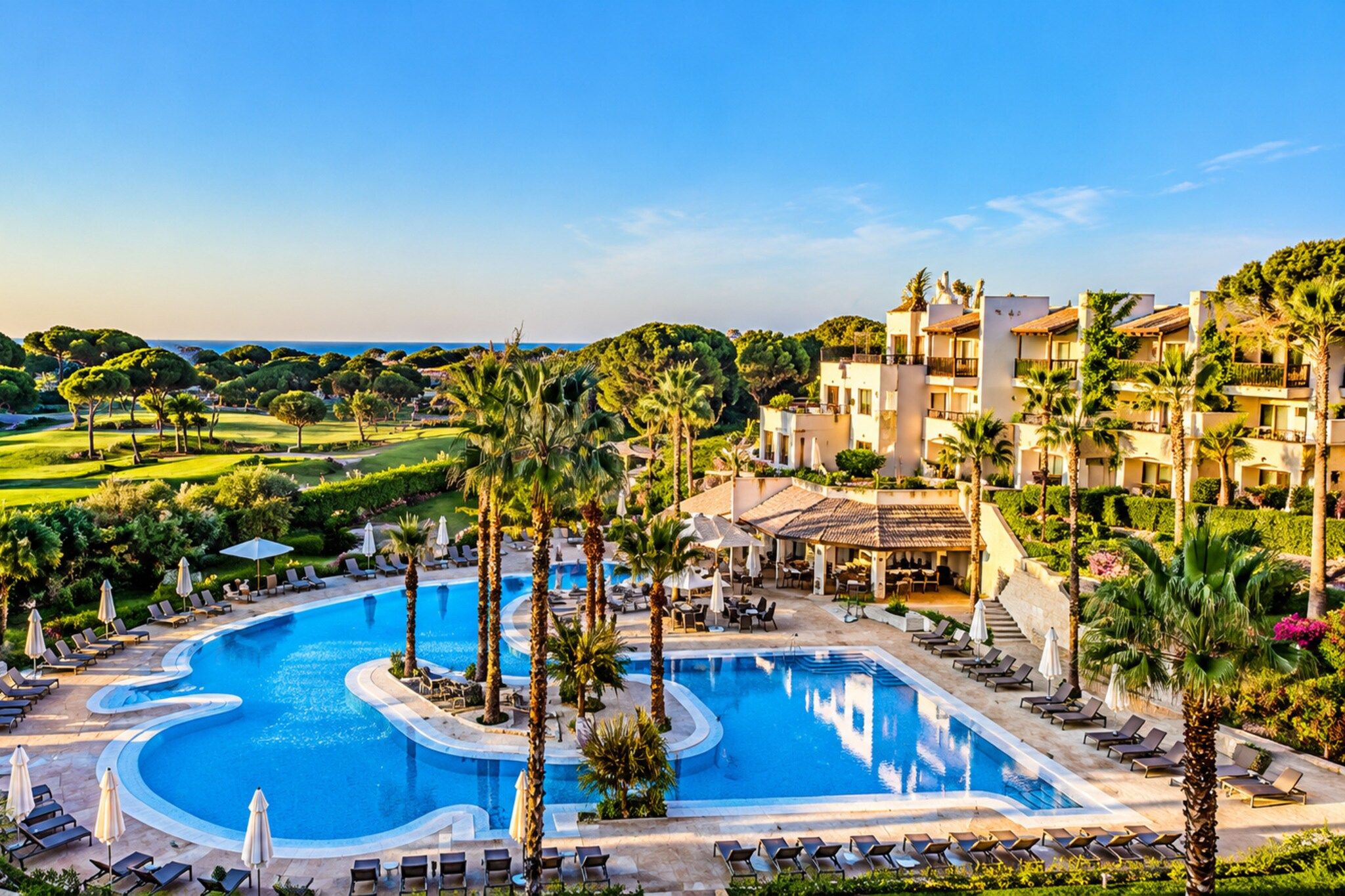 Un resort con una piscina grande, palmeras y un campo de golf al fondo.