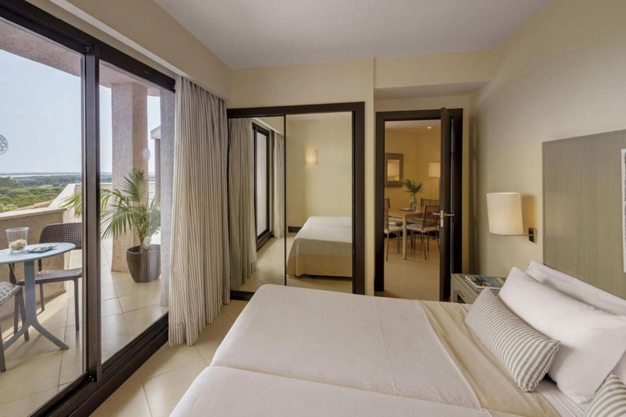 Una habitación de hotel con una cama grande, un rincón de comedor y un balcón con mesa y sillas.
