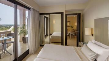 Una habitación de hotel con una cama grande, un rincón de comedor y un balcón con mesa y sillas.