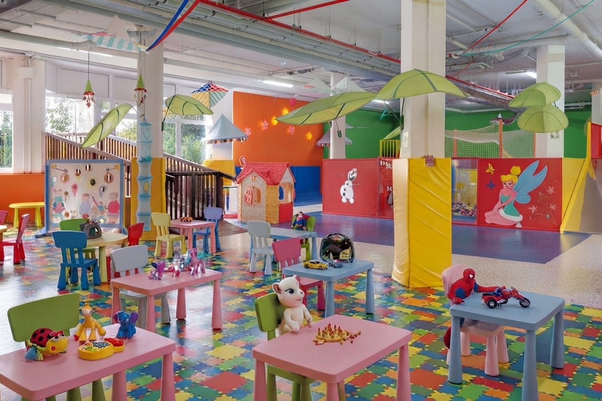 A colorful indoor play area with tables, chairs, and play structures.