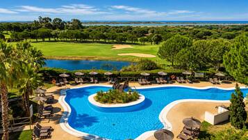 Un resort con una amplia piscina, tumbonas y un campo de golf al fondo.