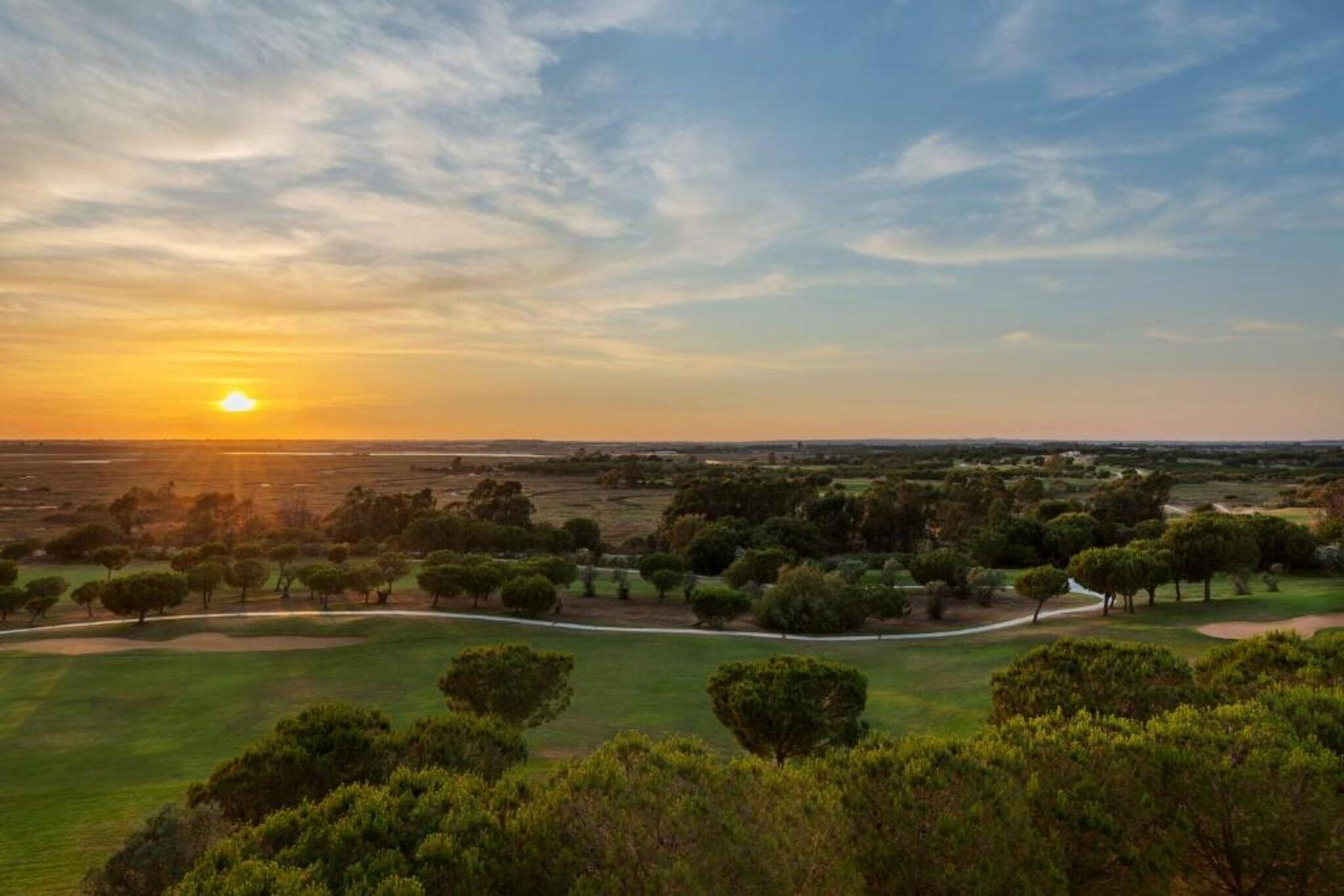 Un parcours de golf offrant une vue imprenable sur le coucher de soleil, entouré d’arbres et de vastes champs ouverts.