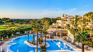 Ein Resort mit großem Pool, Palmen und einem Golfplatz im Hintergrund.