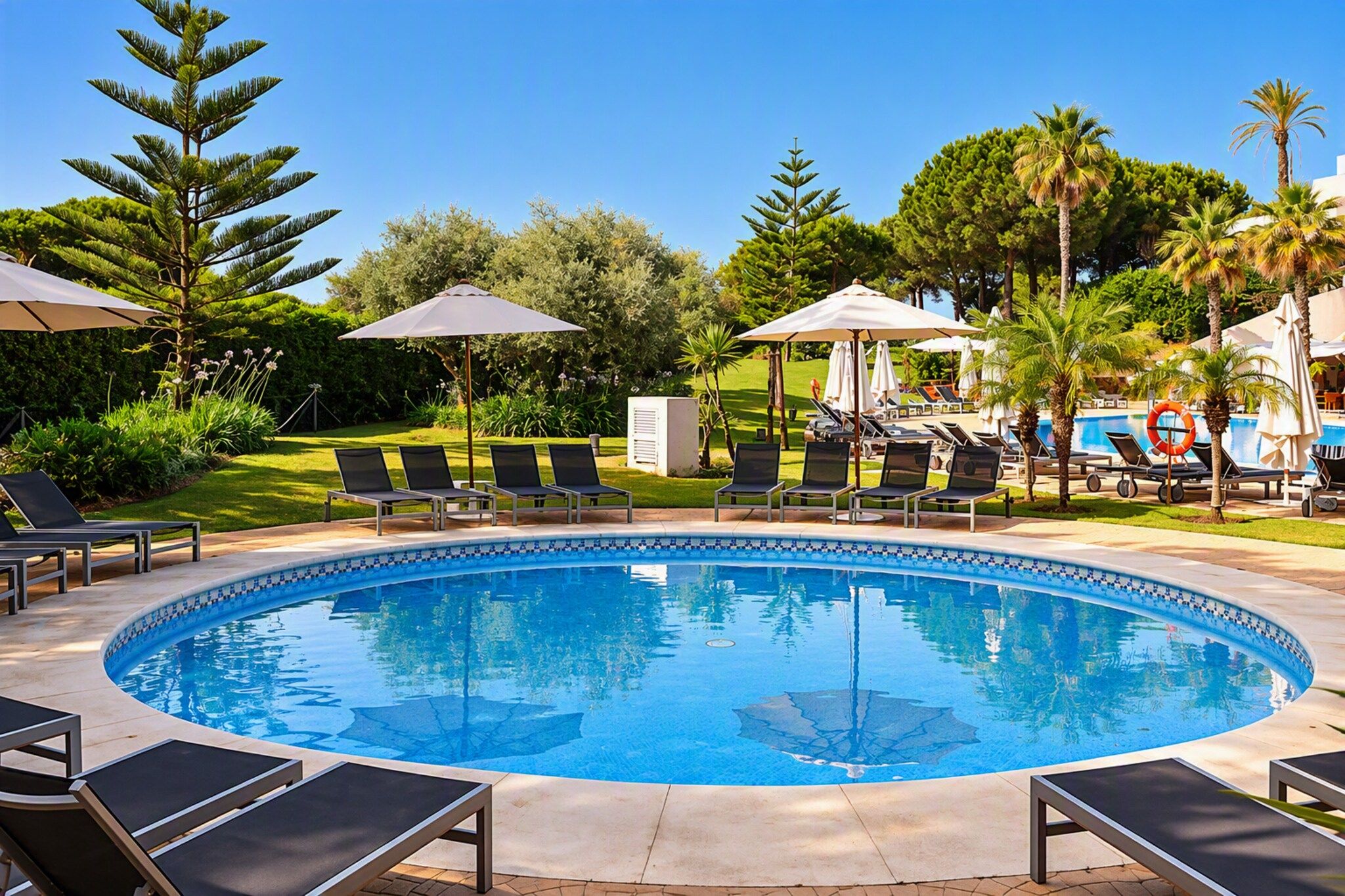 A pool area with lounge chairs and umbrellas, surrounded by greenery and trees.