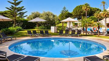 A pool area with lounge chairs and umbrellas, surrounded by greenery and trees.