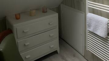 Een slaapkamer met dakraam, een houten balk, een radiator en een witte dressoir met laden.