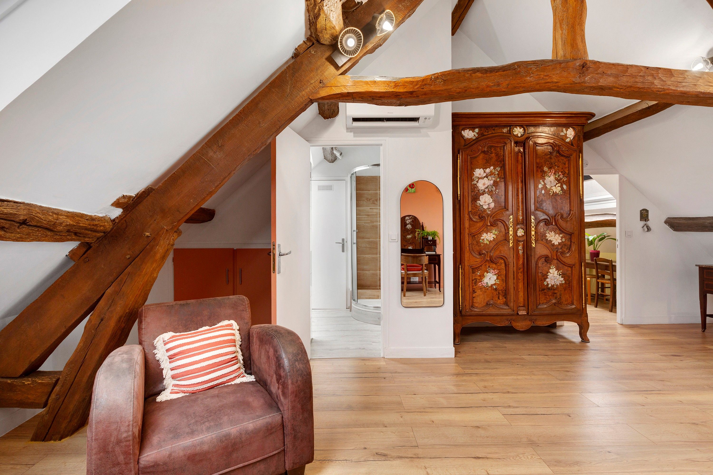 A room with a sloped ceiling, a wooden chair with a striped cushion, and a wooden cabinet with floral carvings.