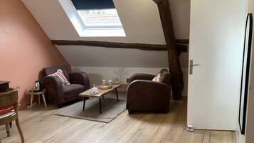 Een loft-achtige kamer met een schuine kap, dakraam, houten balken, een bank, een salontafel en een deur.