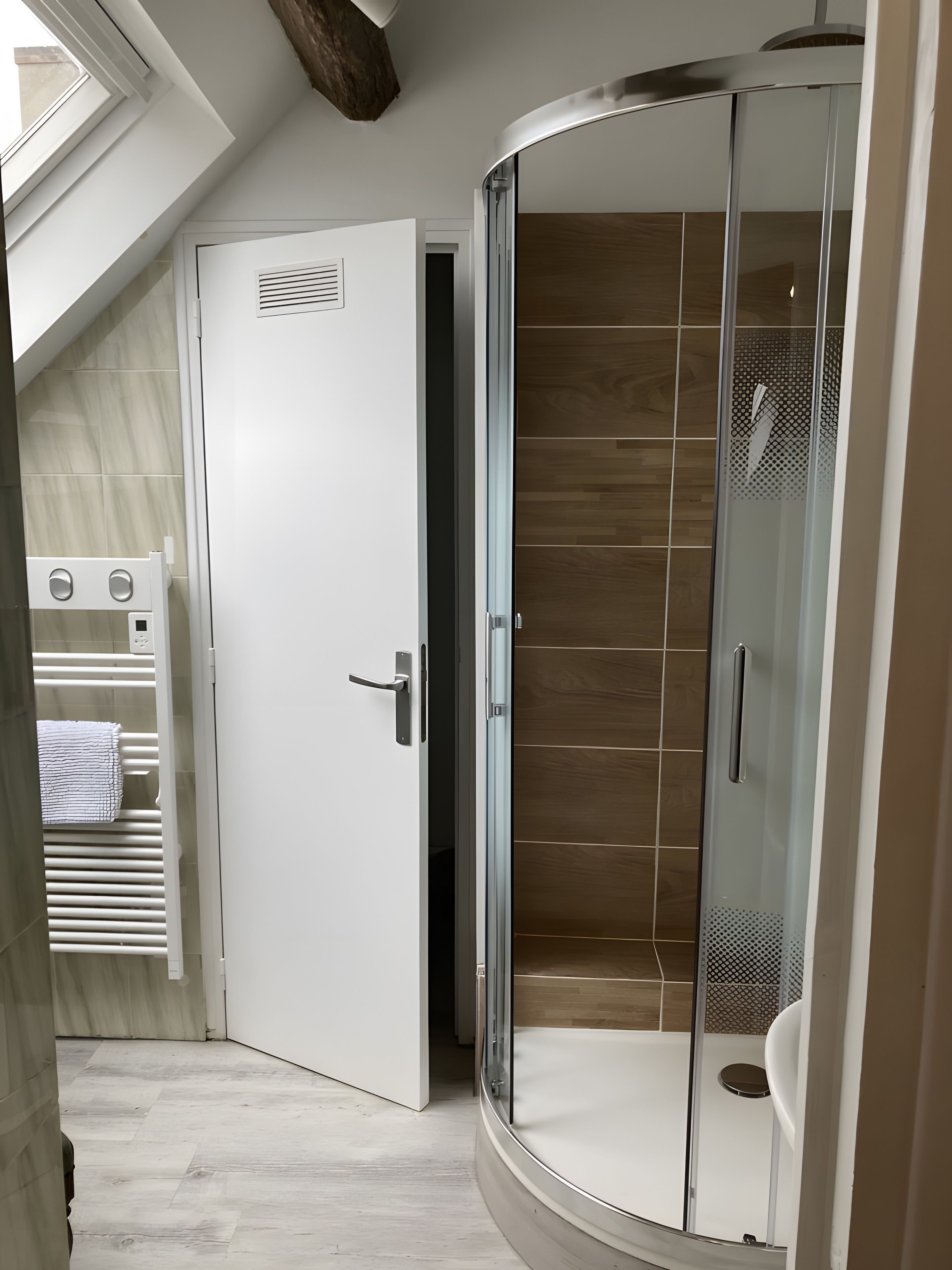A modern bathroom with a glass shower enclosure, a white door, and a towel rack.