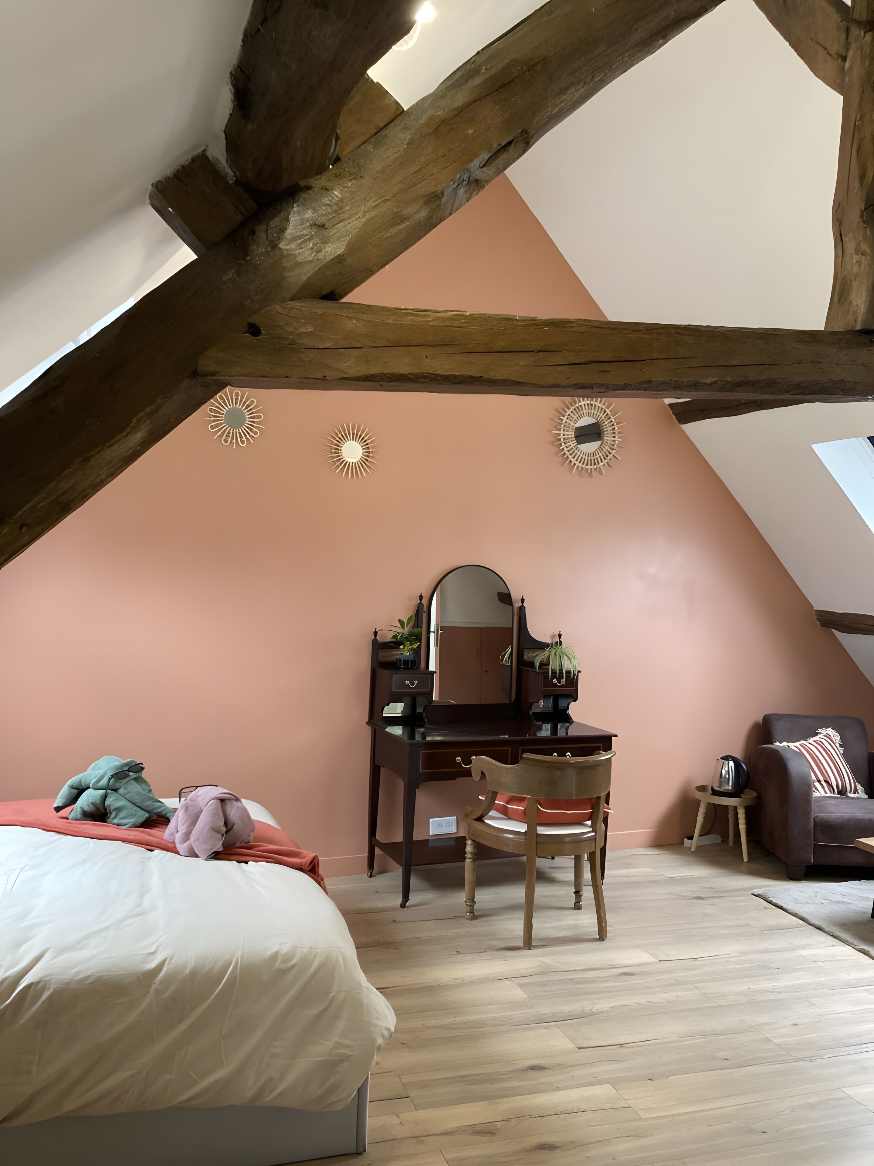 Een slaapkamer met een schuine kap, een houten bureau met spiegel, een stoel, een bed en een klein tafeltje met waterkoker.