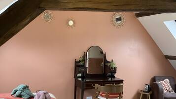Een slaapkamer met een schuine kap, een houten bureau met spiegel, een stoel, een bed en een klein tafeltje met waterkoker.