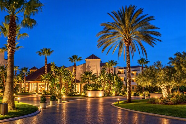 A resort with palm trees, a paved walkway, and buildings with warm lighting.