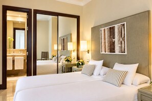 A hotel room with a large bed, a bathroom with a mirror, and a painting on the wall.