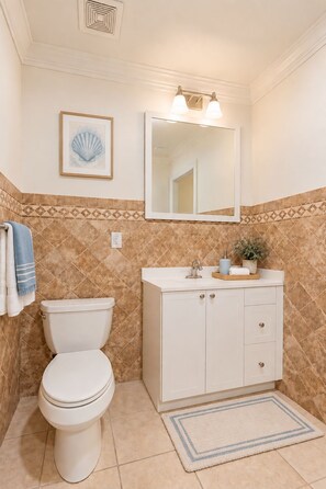 A bathroom with a toilet, sink, mirror, and decorative tiles. - Naples Retreat / 2-Bedroom Apartment (Naples)