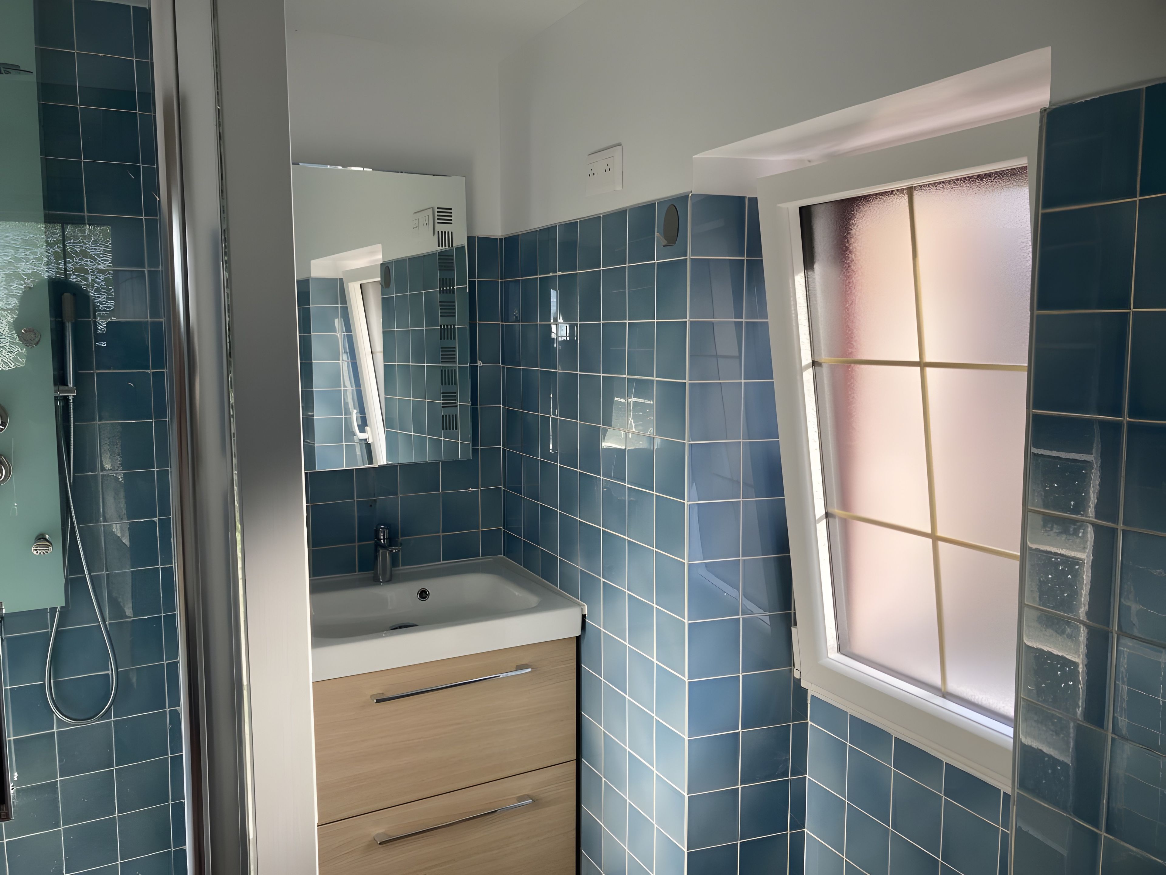 Een badkamer met blauwe tegels, een wastafel, een spiegel en een raam.