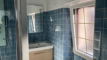 Een badkamer met blauwe tegels, een wastafel, een spiegel en een raam.