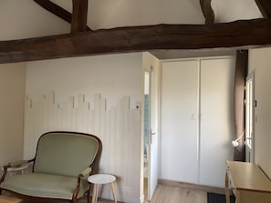 A room with a wooden ceiling, a green upholstered chair, a small round table, a wardrobe, and a window with curtains. - Guest Room 'La Parenth'aise Du Vexin' with Wi-Fi and air conditioning (Saint-Martin-la-Garenne)