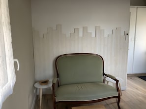 A room with a wooden-framed armchair, a small round table, and a white wall with a geometric pattern. - Guest Room 'La Parenth'aise Du Vexin' with Wi-Fi and air conditioning (Saint-Martin-la-Garenne)