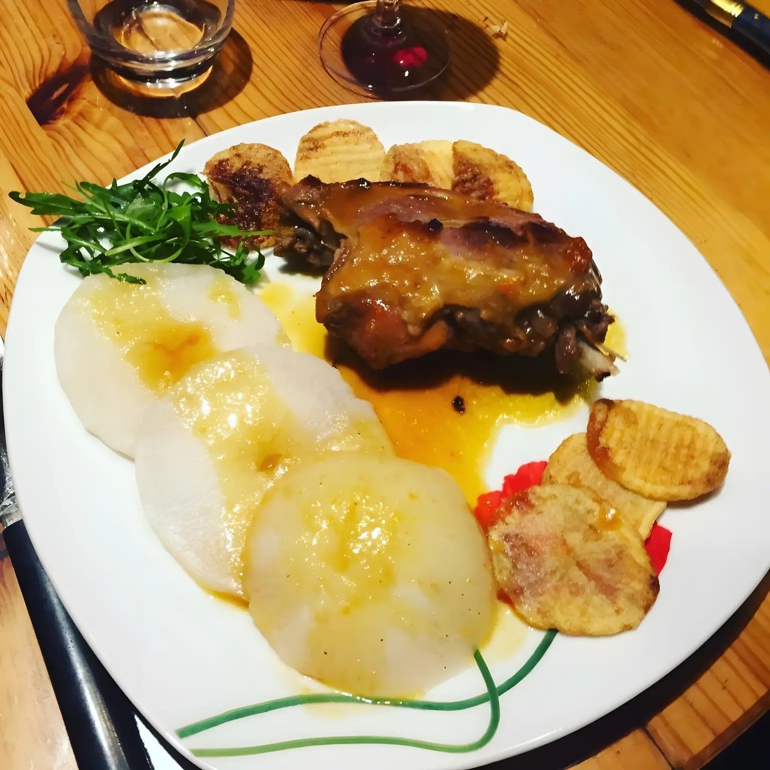 Een bord met gebraden vlees, twee gekookte aardappelen en een portie groenten.