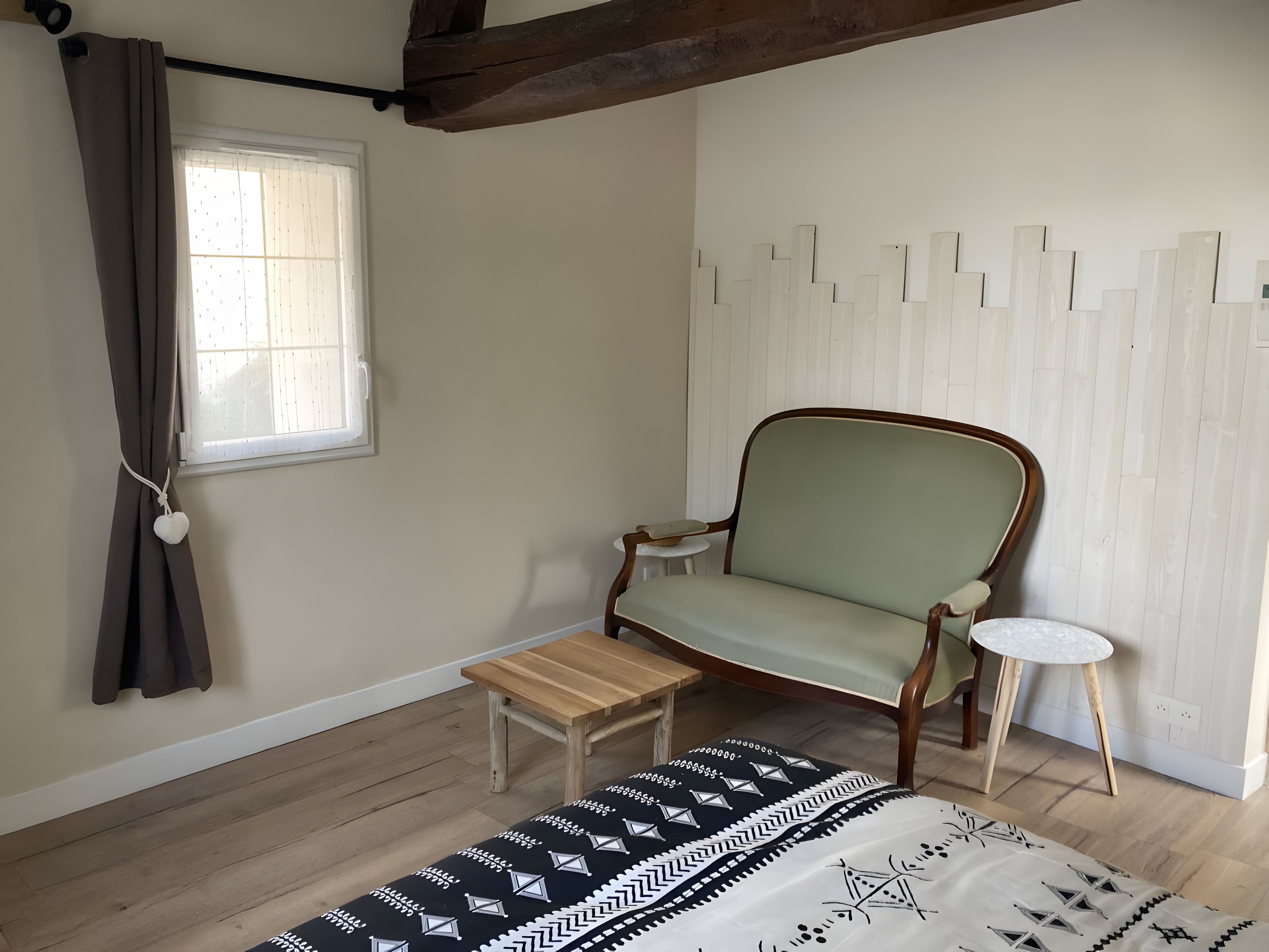Een kamer met een houten vloer, een met groen bekleden stoel, een klein houten tafeltje, een wit rond bijzettafeltje en een vloerkleed met een patroon.
