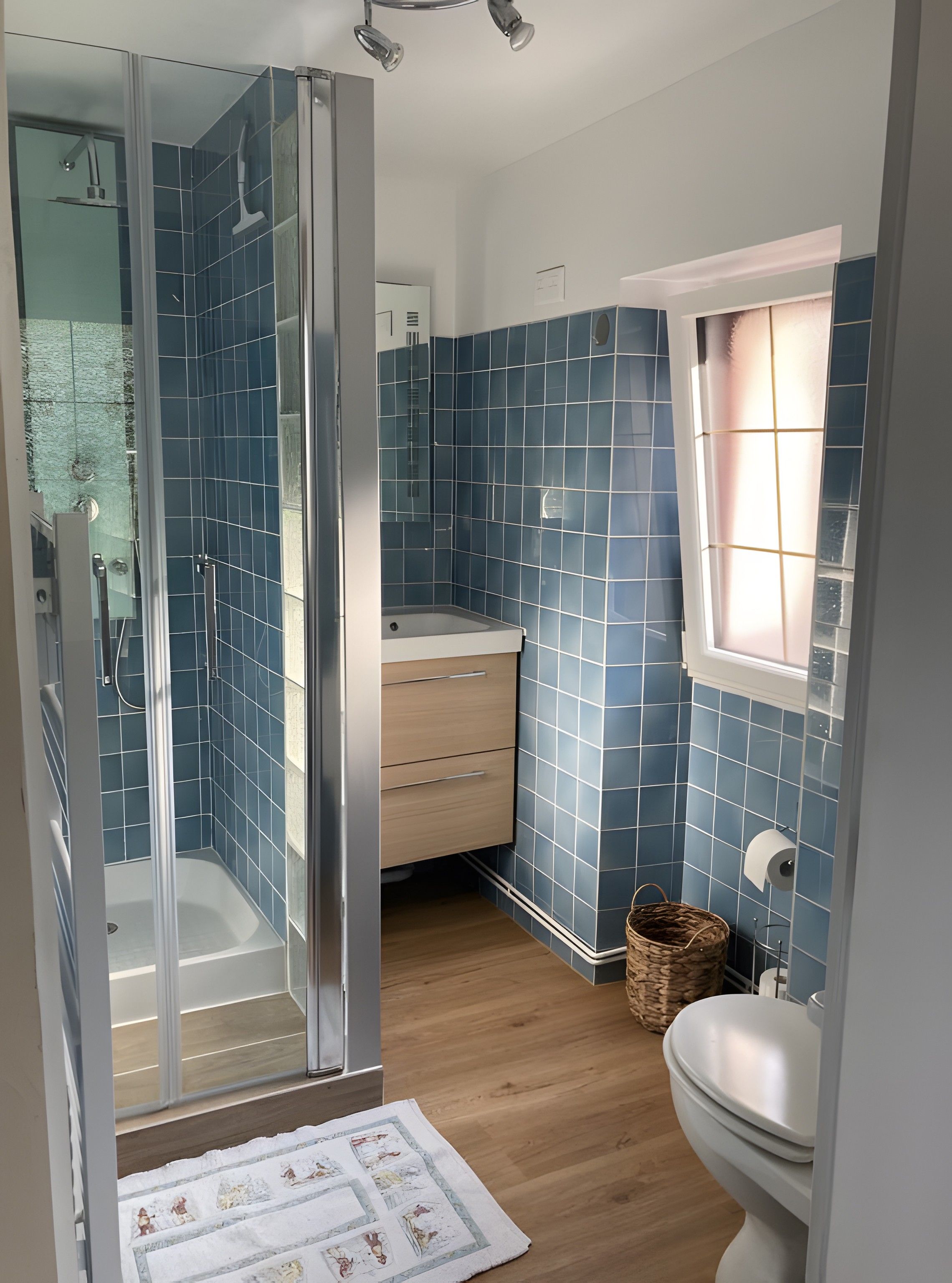 Een badkamer met een douchecabine, toilet, wastafel en een raam.